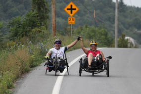 two people riding recumbent trikes on a paved road in summer