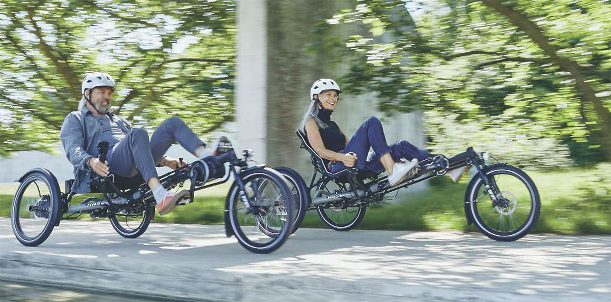 A couple riding Hase Kettwiesel EVO STEPS recumbent e-trikes on a bike path