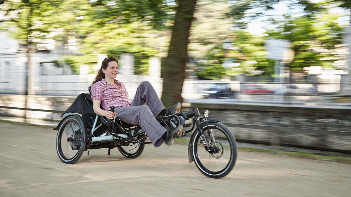 A woman riding a Hase Kettwiesel EVO STEPS recumbent trike in an urban area