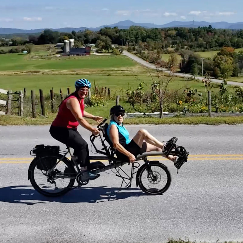 Two women riding a Hase Pino tandem bike in the countryside