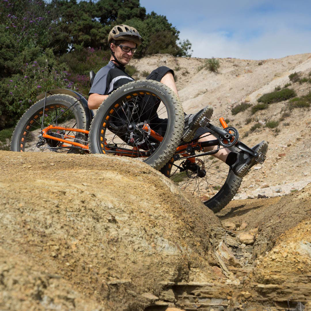 A man riding an ICE Full Fat recumbent trike over rocky terrain