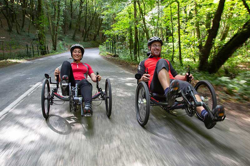 A woman and a man each riding an ICE Sprint X Tour recumbent bike on a country road