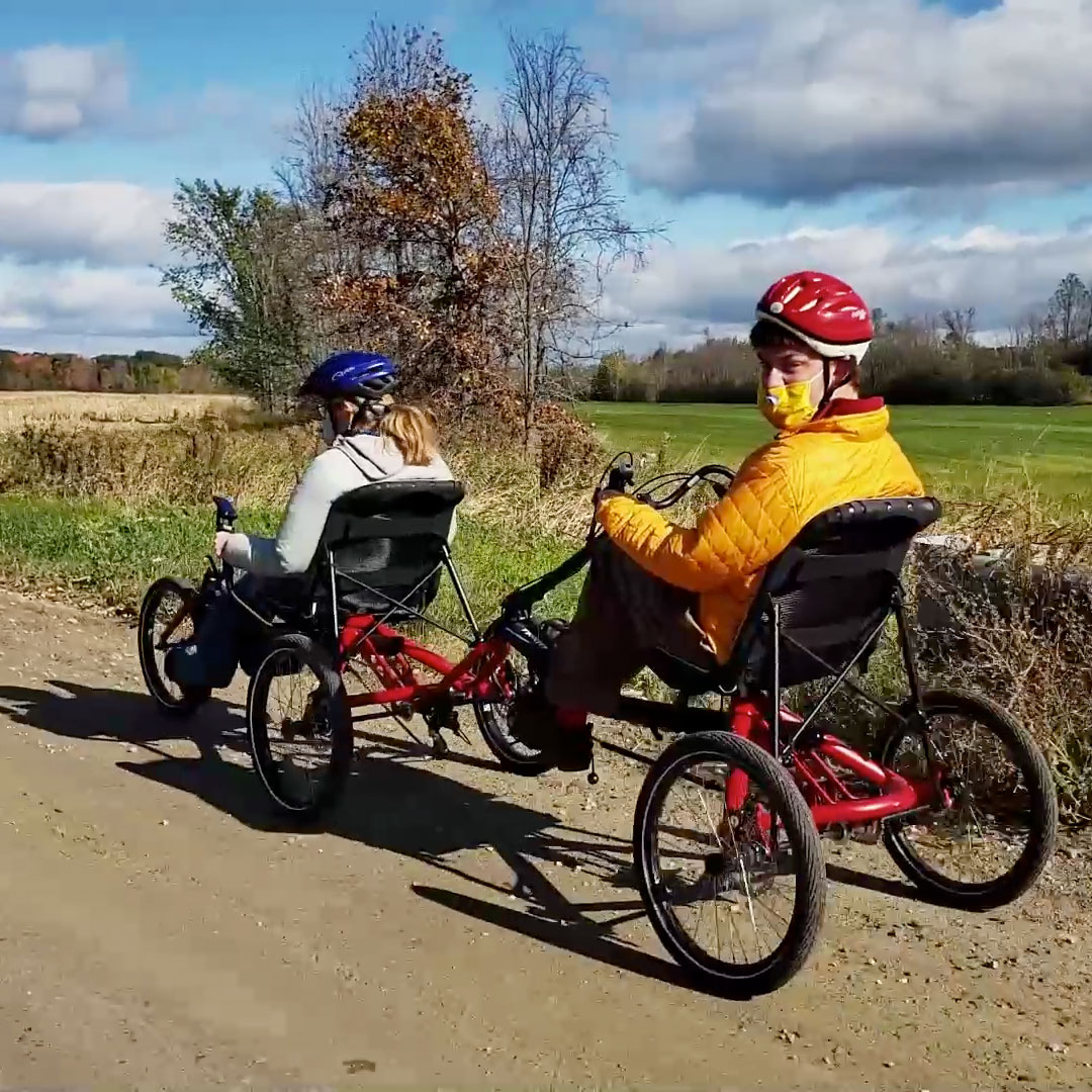 Two people riding two Hase Bikes Trigo recumbent trikes in tandem
